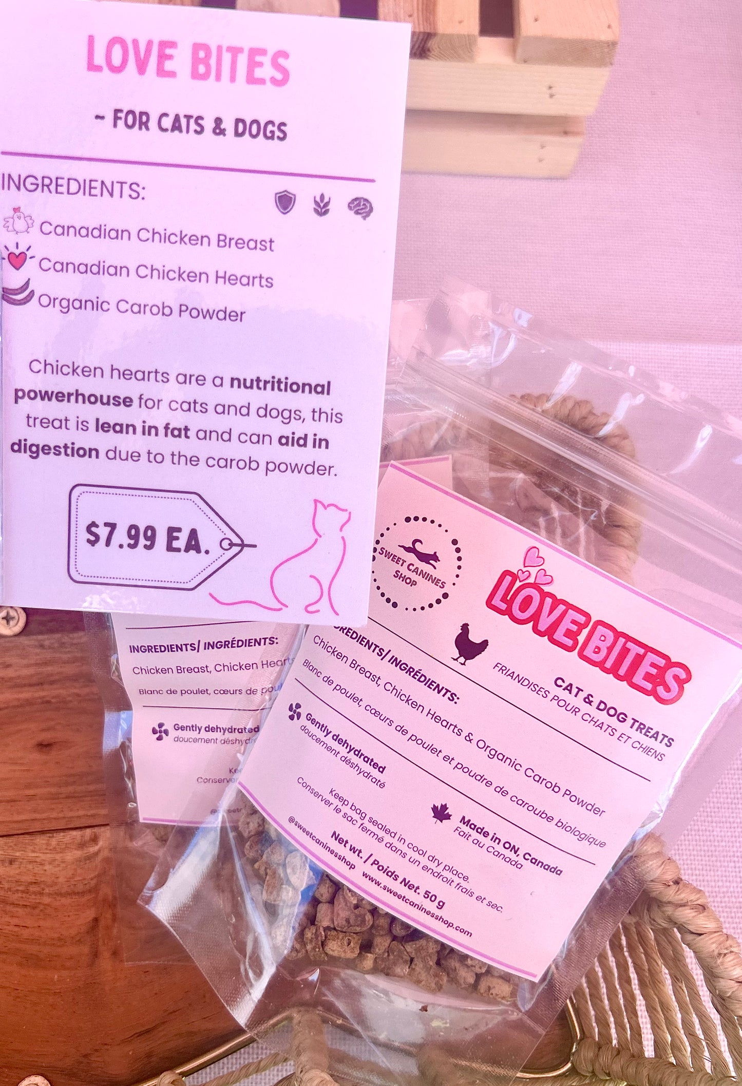 Two clear plastic bags of Love Bites cat and dog treats with pink labels, displayed on a wooden surface with a product information card in the background.