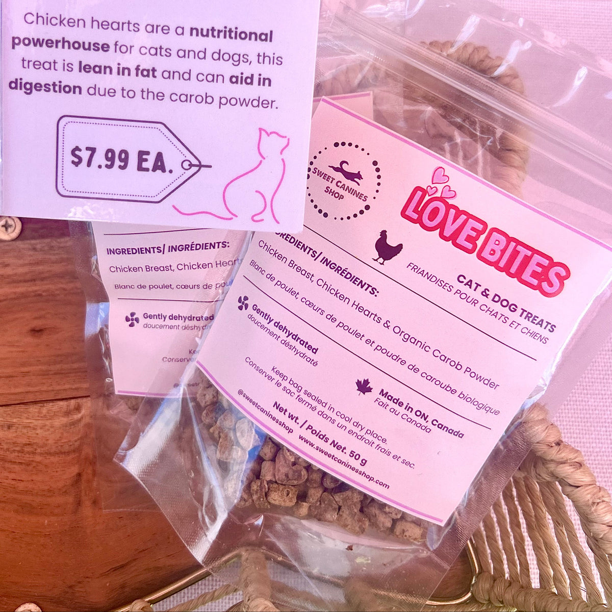 Two clear plastic bags of Love Bites cat and dog treats with pink labels, displayed on a wooden surface with a product information card in the background.