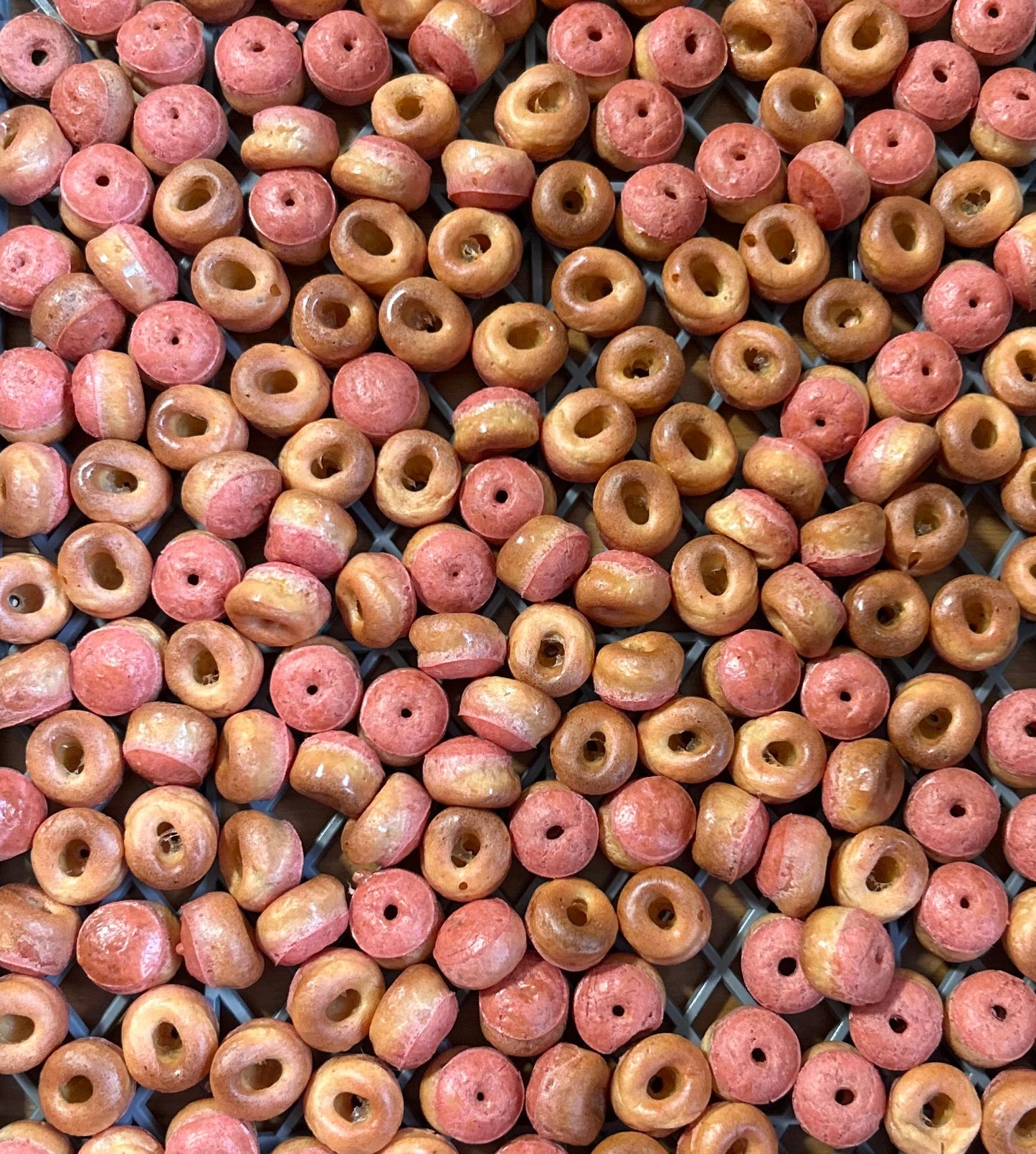 A dense arrangement of small, round, ring-shaped beads with a central hole, featuring a mottled color pattern of pinkish-red and warm tan.