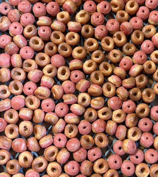 A dense arrangement of small, round, ring-shaped beads with a central hole, featuring a mottled color pattern of pinkish-red and warm tan.