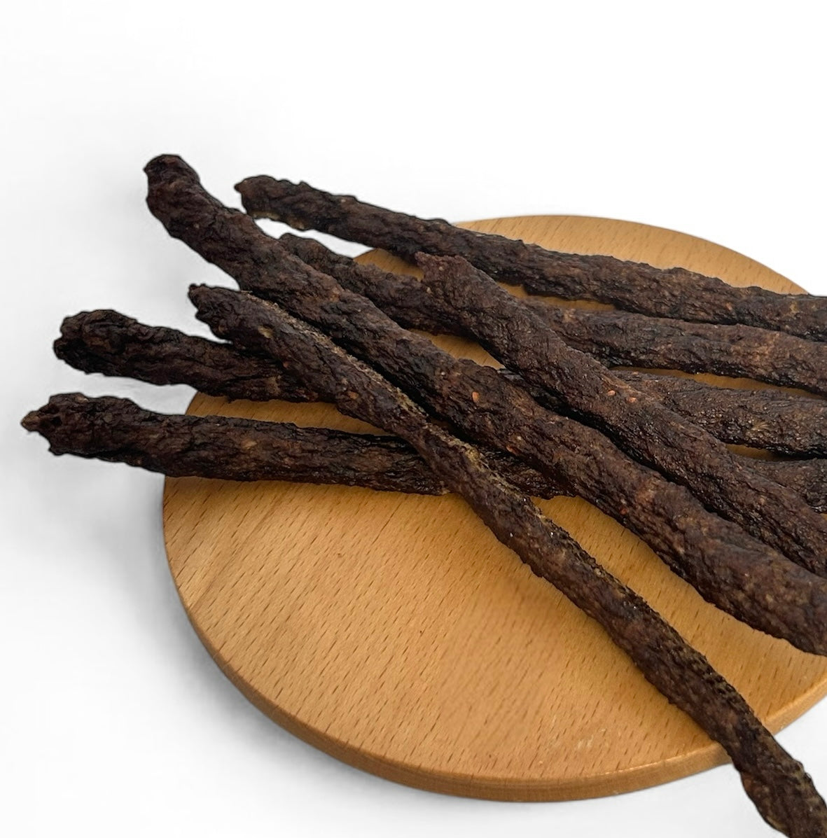 Dark brown dried jerky sticks arranged on a round light wood plate against a plain white background.