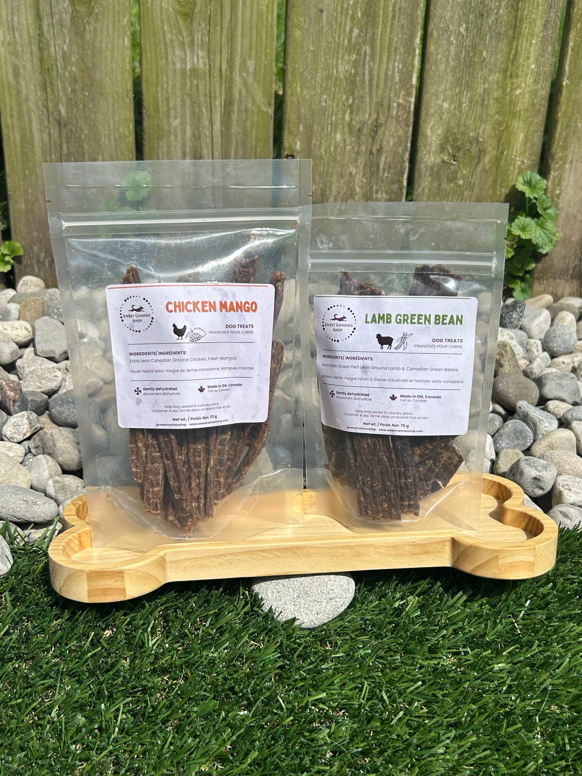 Two packages of pet food with labels on a wooden surface next to a stone path and grass.