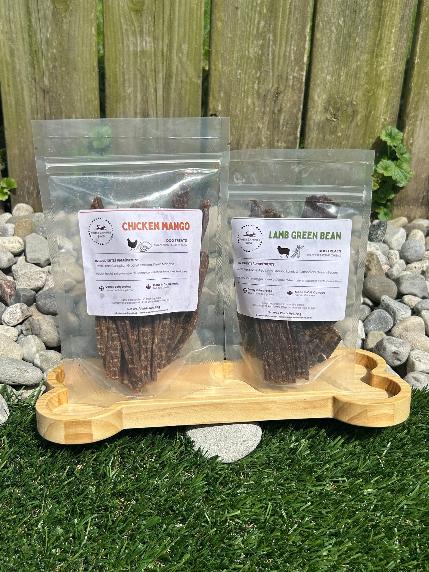 Two packages of pet food with labels on a wooden surface next to a stone path and grass.