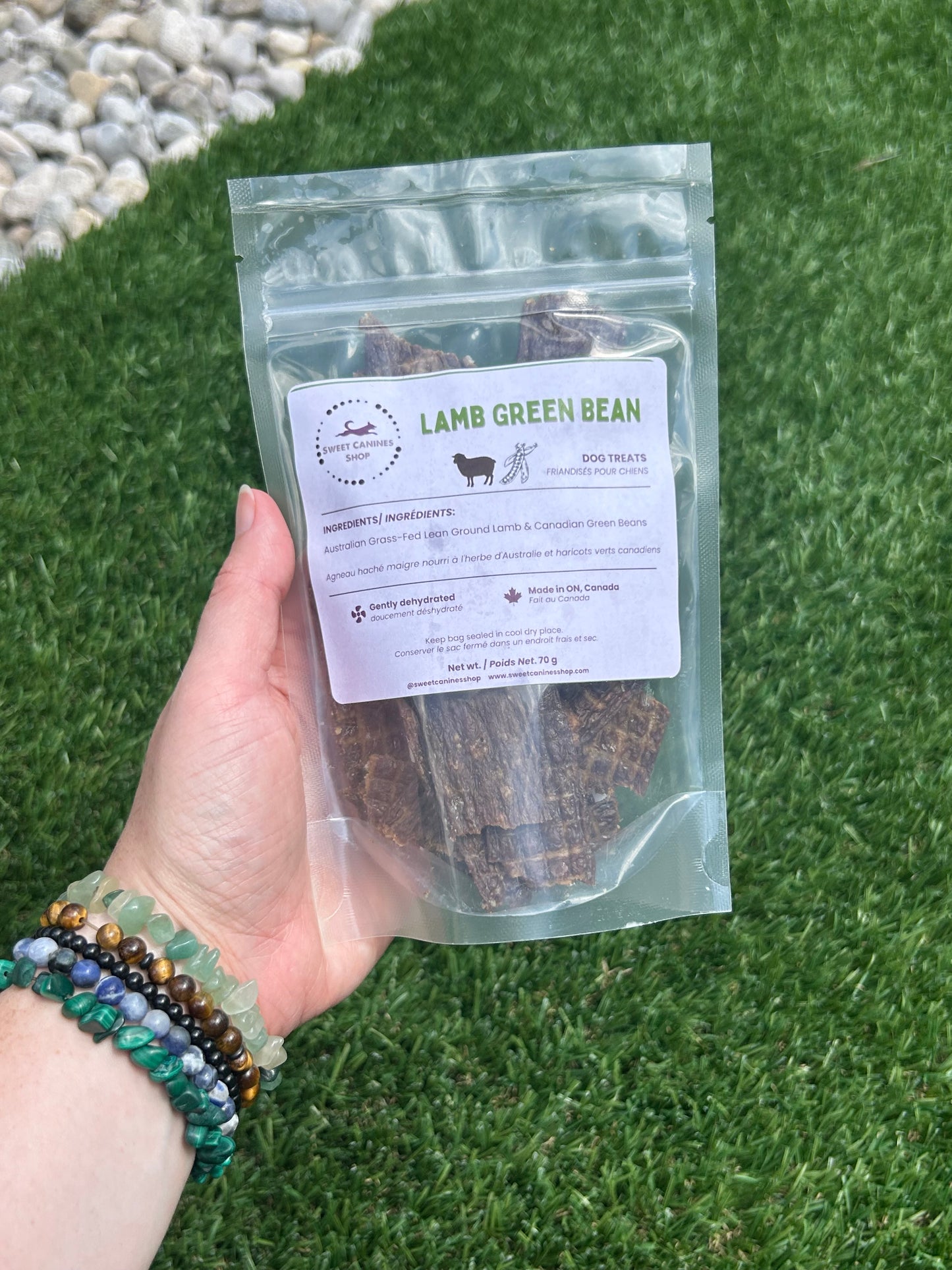 Hand holding a package of lamb and dried green beans with a label against a grass background